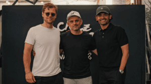 Three men posing together in front of a black-branded backdrop.