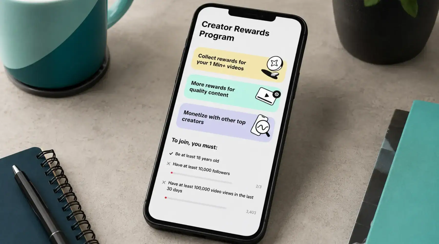 Image displaying a phone on a desktop and on its screen its the TikTok Creator Rewards Program.