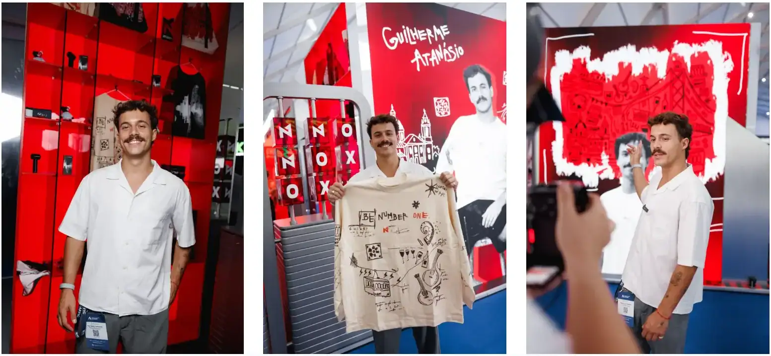 Man at a red-and-black fashion display holding an illustrated shirt and posing beside matching artwork.